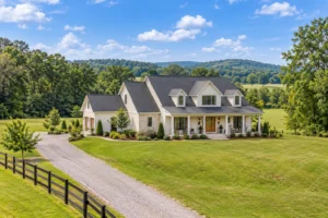 Farmhouse with a covered porch, open acreage, and a wooded backdrop.